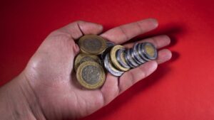 manos sosteniendo monedas con fondo mexicano