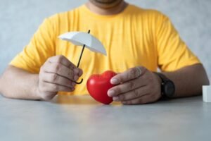 manos sosteniendo un corazon protegido por paraguas
